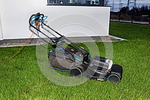 Electric lawn mower with electric drive with a cutting width of 44 centimeters standing on the lawn in the evening.