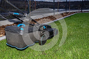 Electric lawn mower with electric drive with a cutting width of 44 centimeters standing on the lawn in the evening.