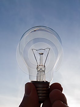 Electric light bulb in hand against the blue sky during a sunny evening