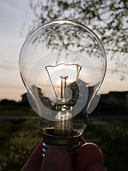 Electric light bulb in hand against the sun during the evening