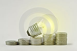 Electric light bulb on raising piles of coins -  Concept of increase in electricity bills