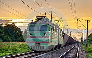 Electric locomotive hauling a cargo train at sunset