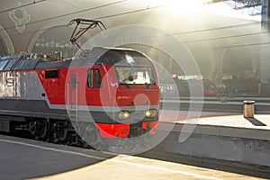 Electric locomotive at the terminal passenger station under the roof, illuminated by the sun`s rays