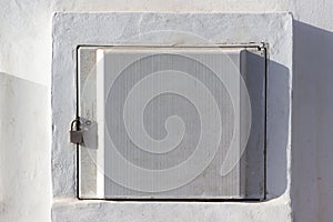 Electric meter box locked with padlock on white wall