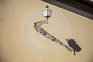 Electric old fashioned lamp light with a long shadow mounted on historic facade in Italy.