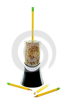 Electric pencil sharpener with a yellow pencil sticking out of it, filled to the brim with pencil shavings, isolated on