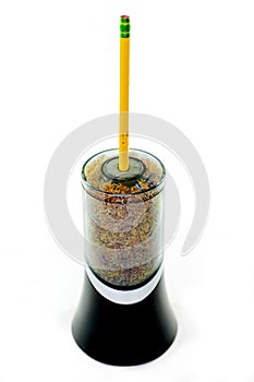 Electric pencil sharpener with a yellow pencil sticking out of it, filled to the brim with pencil shavings, isolated on