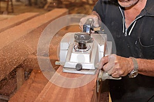 Electric planer is being worked with hands of senior carpenter in carpentry workshop. Selective focus and shallow depth of field.