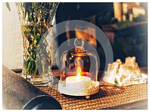 An electric candle burning under a glass on table