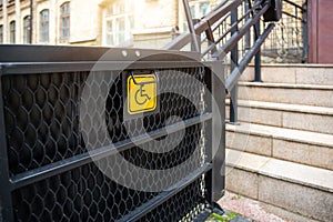Electric platform lift at building staircase for disabled people with wheelchair sign plate on old city street. Elevator