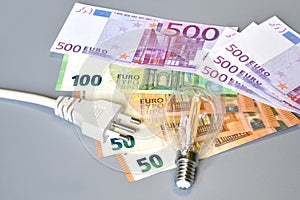 Electric plug, light bulb and euro money banknotes over grey background. Concept for the increase of electricity cost.