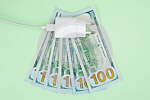 Electric plug with a wire against the background of spread out one hundred dollar bills