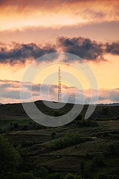 Electric pole on top of a hill with vibrant orange light in the background during sunrise.