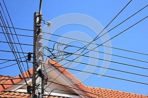 Electric pole and wire cable on blue sky,The roof of the house in the background