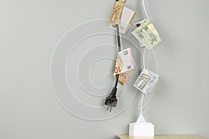 Electric power cord with Euro banknotes plugged into power outlet socket. Energy efficiency, power consumption