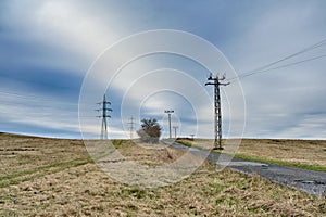 Electric power grid frame pylons and transmission towers along rural road in grasslands of Czechia