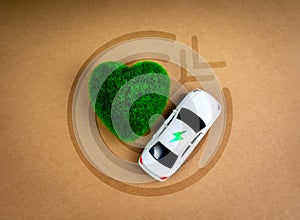 Electric power icon on white car near green heart-shape on target symbol on brown kraft paper background.