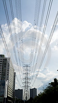 Electric power line with high voltage tower at far sight and building around with blud sky and cloud.