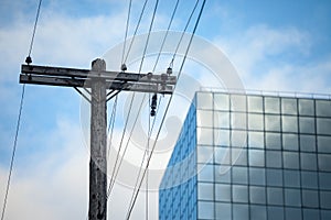 Electric power line, old and outdated, on a rotten wooden pole, facing and supplying energy to a modern office building