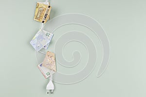 Electric power plug with Euro banknotes hanging on light green background. Energy efficiency, power consumption