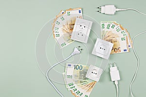 Electric power plugs and electric sockets with Euro banknotes on light green background. Electricity cost and expensive