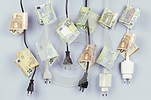 Electric power plugs with Euro banknotes on them hanging on light blue background. Energy efficiency, power consumption