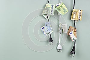 Electric power plugs with Euro banknotes on them hanging on light green background. Energy efficiency, power consumption