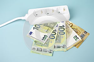 Electric power strip extension cord with Euro money banknotes on light blue background. Increasing electricity cost