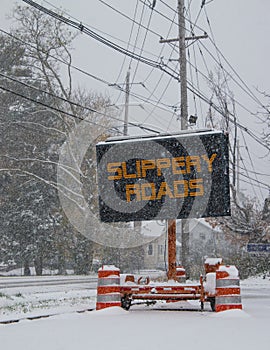 Electric road traffic mobile sign by the side of a snow covered road in winter with snow falling warning of slippery roads.