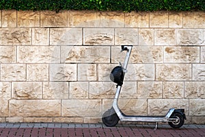 Electric scooter with a helmet stands near a stone wall