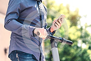 Electric scooter and mobile phone. Business man using e vehicle rent service with smartphone in urban city street and park.