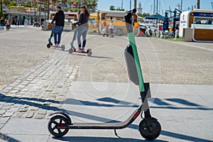 electric scooter roller parked on the sidewalk at the port of Malaga on a sunny day and a blurred couple use them in background photo