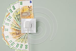 Electric socket with connected power plug and Euro banknotes arround it. Electricity cost and expensive energy concept