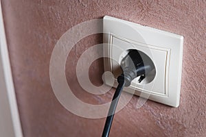 Electric socket on a pink wall. The black wire plug is connected. Renovated backdrop of studio apartment. Blank copy