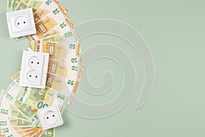 Electric sockets with Euro banknotes on light green background. Electricity cost and expensive energy concept. Top view