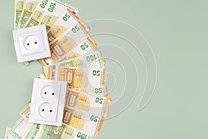 Electric sockets with Euro banknotes on light green background. Electricity cost and expensive energy concept. Top view