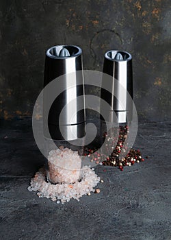 Electric spice mills. Made of metal. Nearby pepper and salt. Grey background