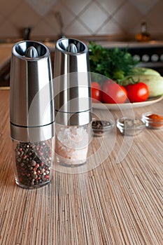 Electric spice mills. Stand on the table on the table. Nearby are cups with spices and vegetables