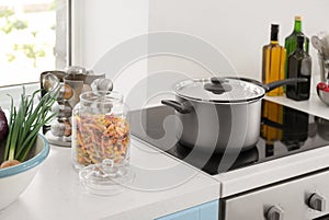 Electric stove with stewpan and products on table in modern kitchen