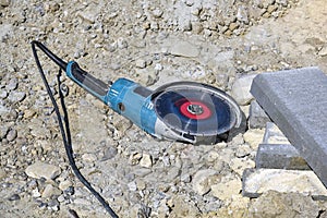 Electric tool with diamond disc for cutting stones lies on gravel. Angle grinder is ready for operation. Stone cutting technology