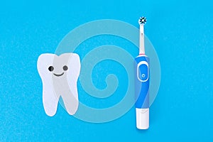 Electric toothbrush, toothpaste, a tooth carved out of felt with a smiling cartoon face. Blue background. Flat lay. The