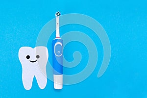 Electric toothbrush, toothpaste, a tooth carved out of felt with a smiling cartoon face. Blue background. Flat lay. The concept of