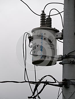 electric transformer of a city utility hanging on a pole with maintenance signs in Spanish