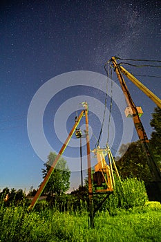 Electric transformer in forest. Night starry sky with glowing stars and meteoric track trail. Power lines in starry sky