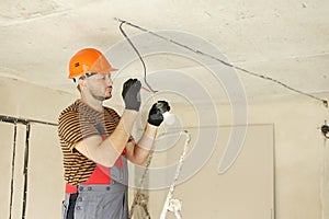 Electric in uniform, protective gloves and hard hat checking and measuring the presence of electrical voltage in bulb