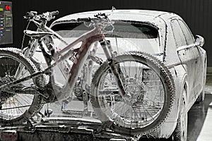 Electric vehicle and bicycles at self-service car wash during nighttime, covered in foam,
