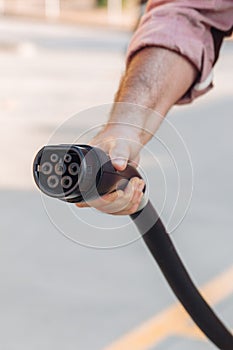 Electric vehicle or EV car socket held by a hand in a charging station. Electrical power supply and Eco-friendly alternative