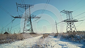 Electric voltage towers, transmission power lines, electricity pylons at sunny winter snow background. Renewable green