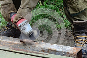 Electric wheel grinding on steel structure outdoors. Old manual worker in protective gloves cutting metal door with grinder