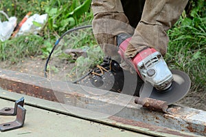 Electric wheel grinding on steel structure outdoors. Old manual worker in protective gloves cutting metal door with grinder
